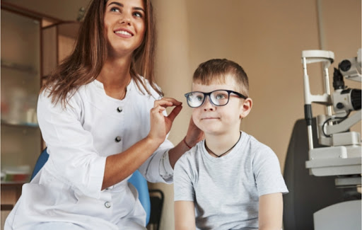 A young female optometrist fits a young boy for a pair of glasses inside the examination room.