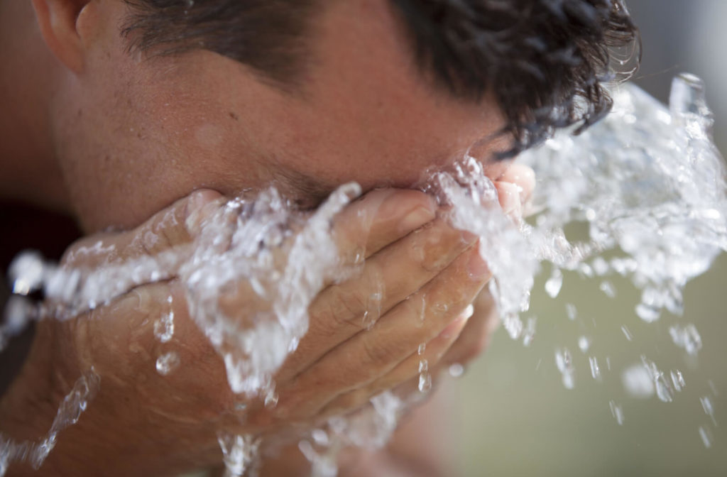 A man washing his sunburned eyes with cold fresh water to soothe the burn and remove any particles that may be causing irritation.