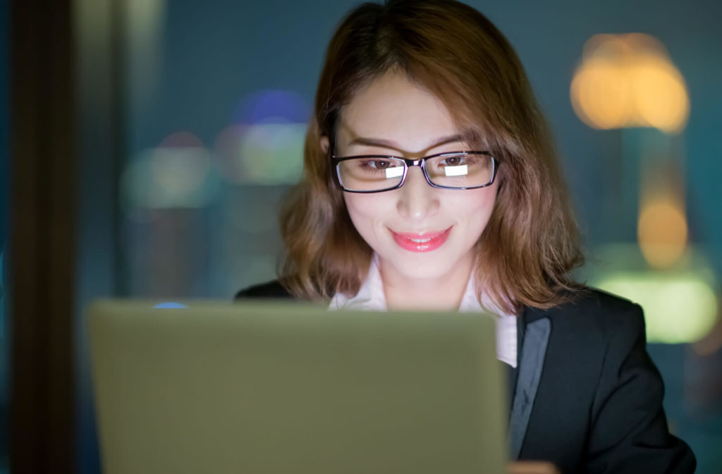 A young woman is wearing blue light glasses while working on her computer at the office.