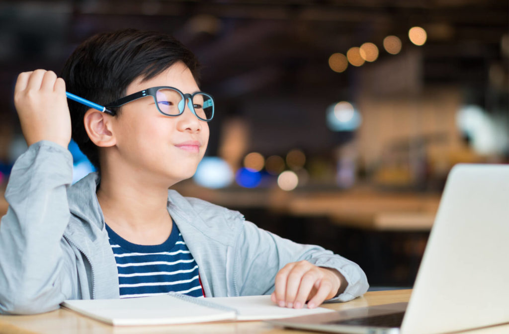 A schoolboy is wearing blue light-blocking eyeglasses in front of his computer during his online class