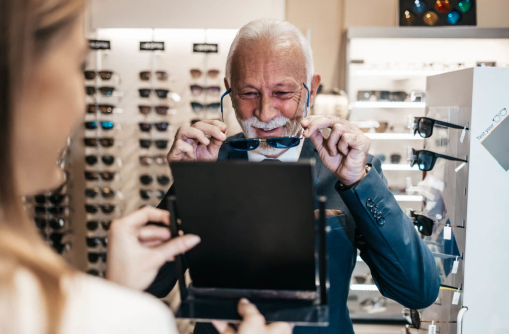 An elderly man is trying on sunglasses in front of a mirror in an optical store.