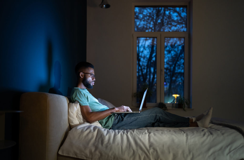 A man using his laptop in a poorly lit room.