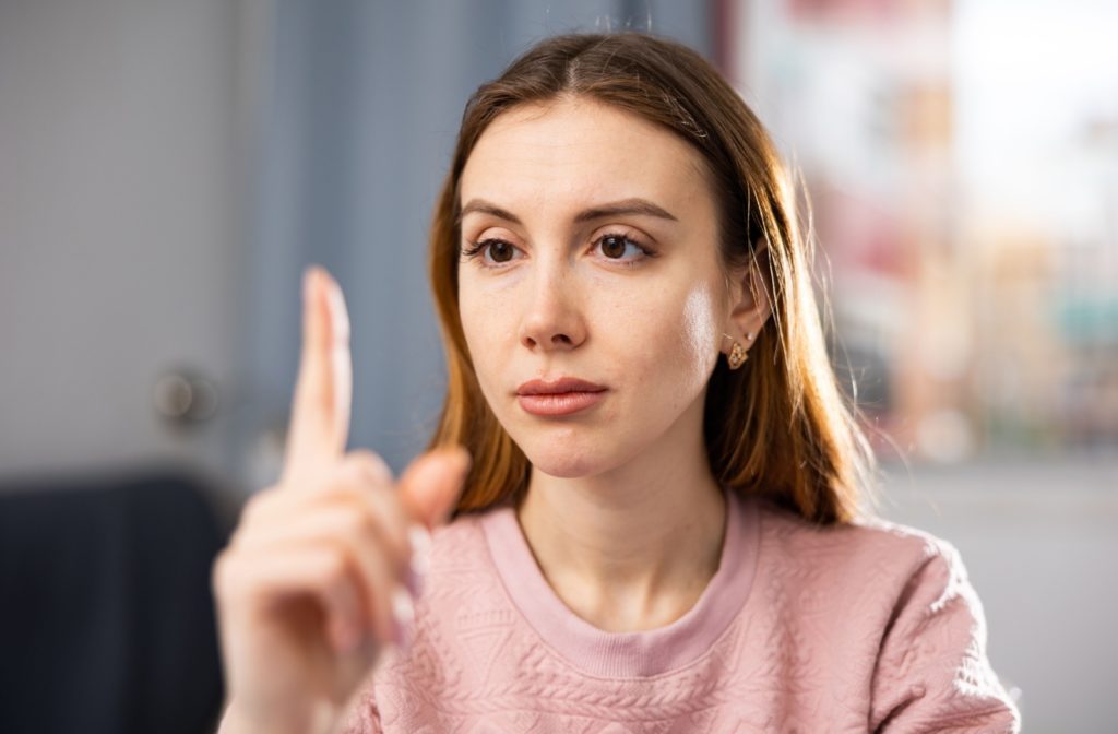 A patient in a pink sweater focuses on her finger while exercising her eyes.