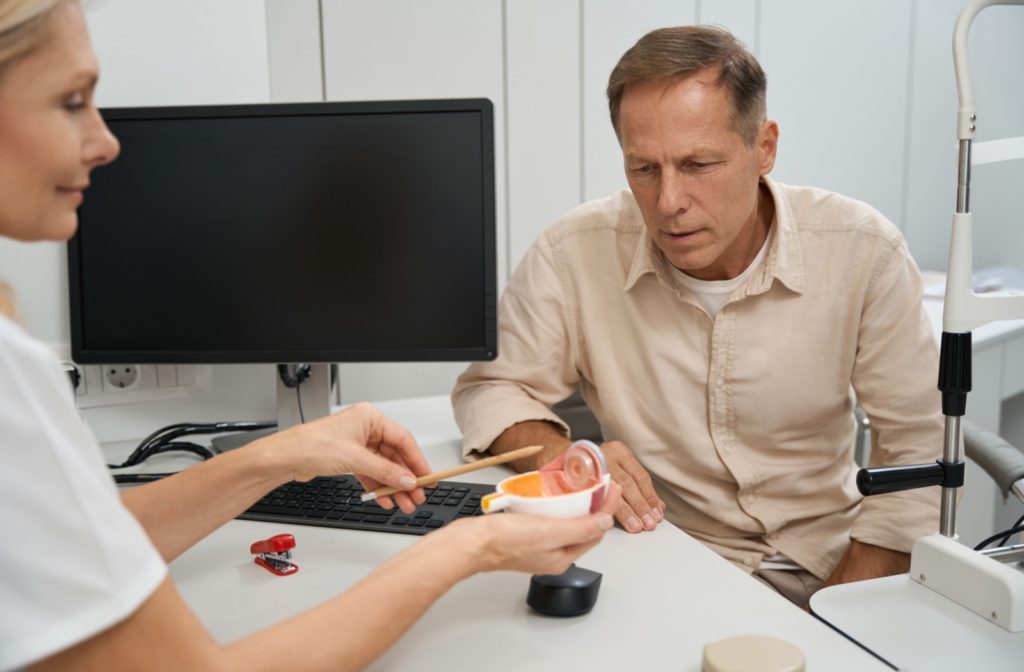 An optometrist shows a patient an eye model to explain where he is experiencing symptoms while in the eye doctor’s office.