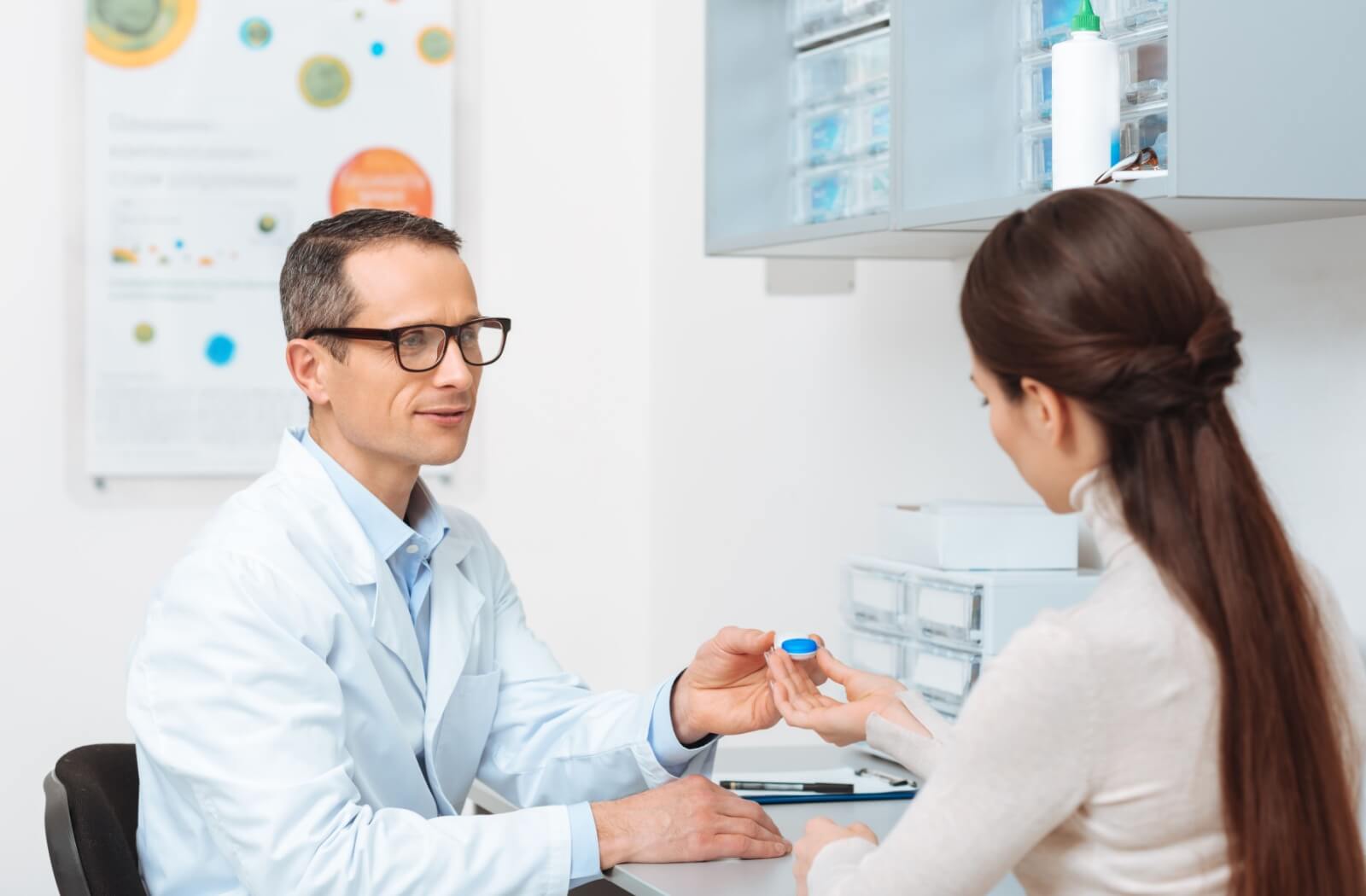 An optometrist discusses proper contact lens wear and care with their patient during a lens fitting.