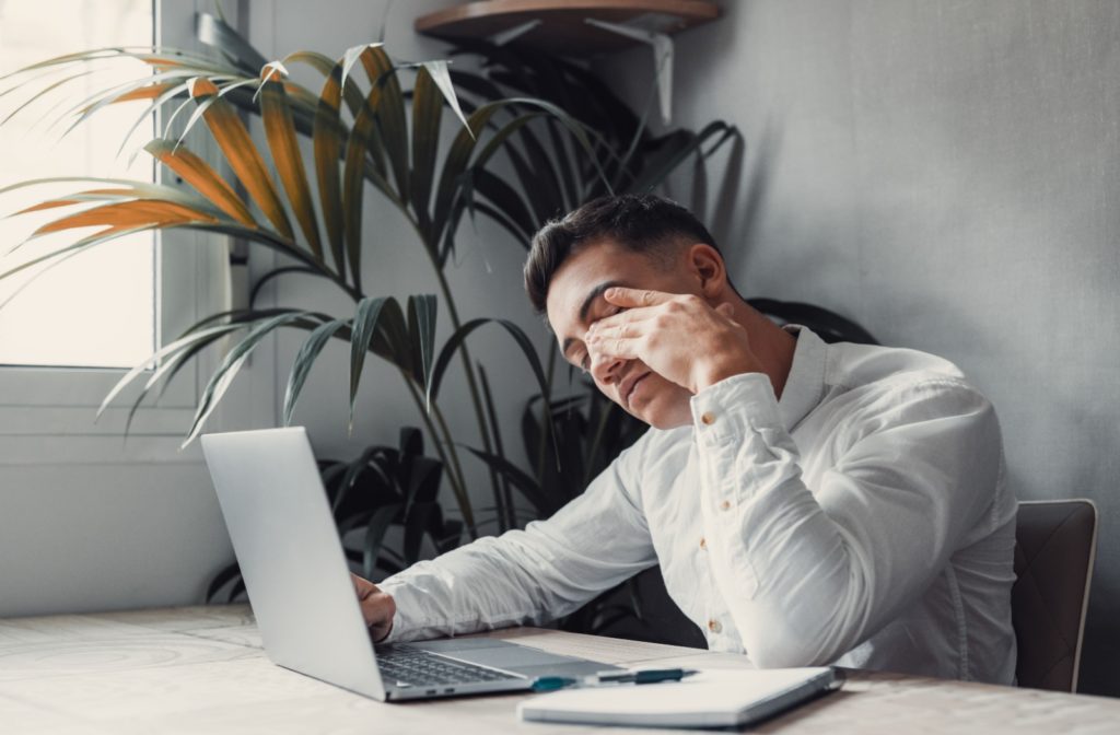 A person working at a laptop rubs their tired eyes.