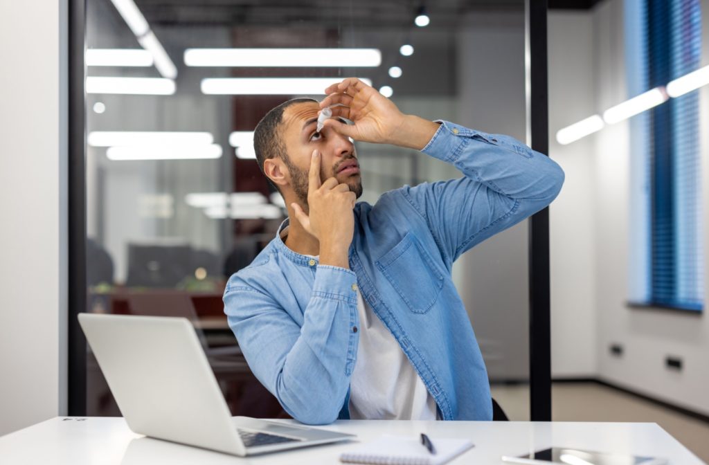 A person uses artificial tears to relieve their dry eyes while at work.