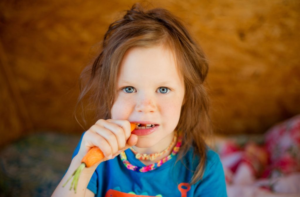 A young child biting into a fresh carrot