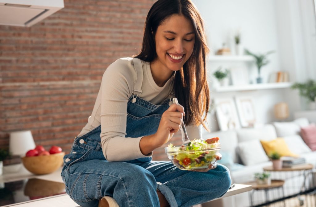 A person sitting on their kitchen counter enjoying eating a salad full of leafy greens to help support their eye health