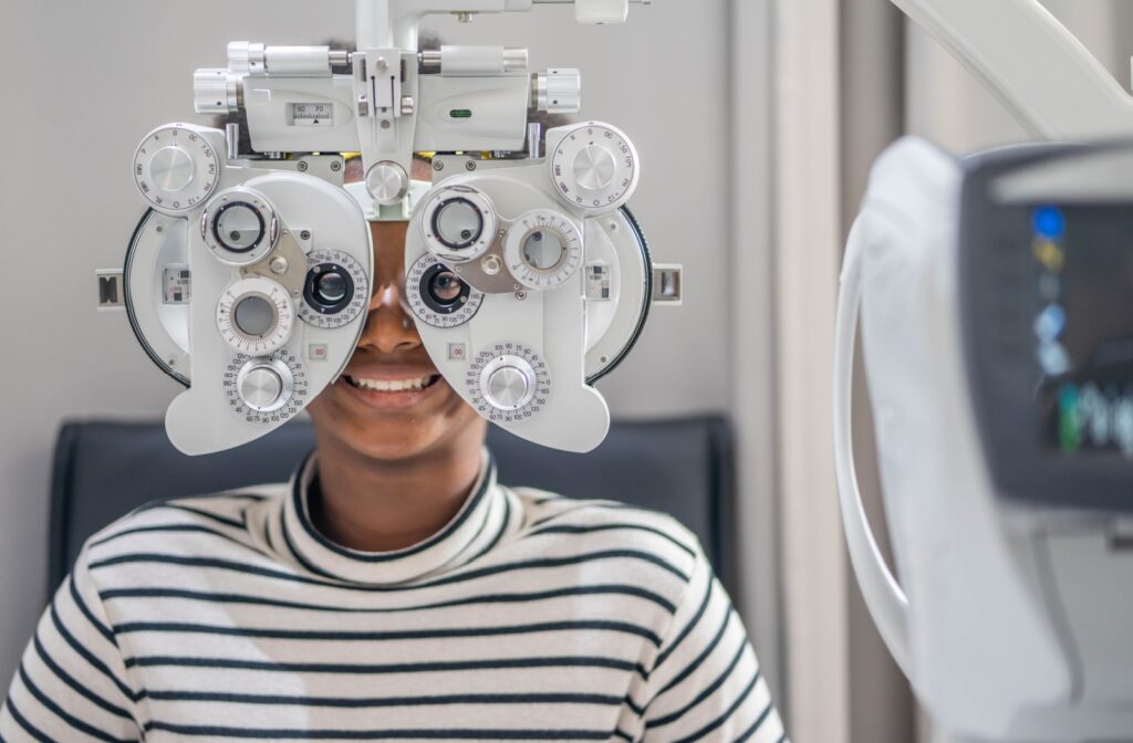 A young patient in a striped shirt smiles behind a phoropter during an eye exam.