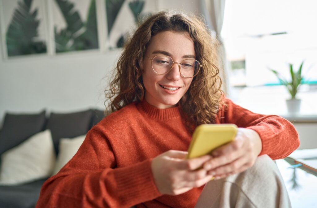 Young smiling woman wearing glasses holding a smartphone.
