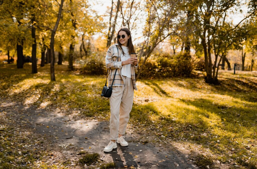 A person standing in a park outside, wearing sunglasses to protect their eyes all year round.