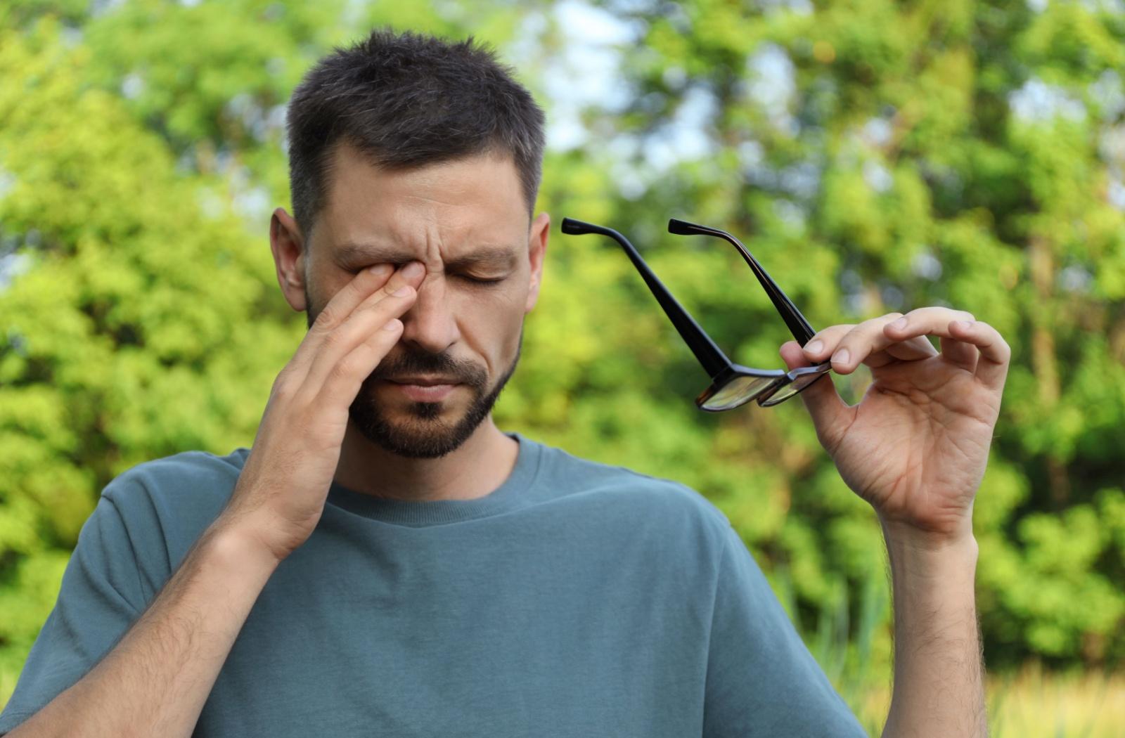 A person outside who removed their glasses to rub their eyes due to allergies.